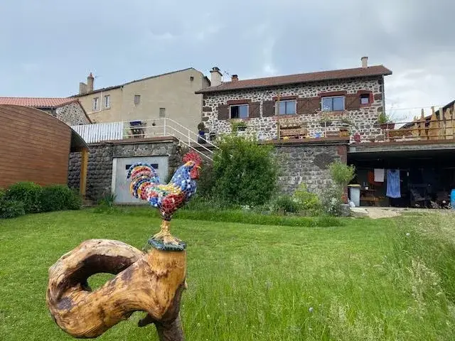 Coq coloré sur pelouse devant maison en pierre