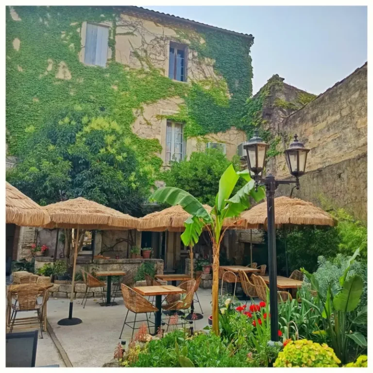 Cour intérieure verdoyante avec café et parasols en chaume