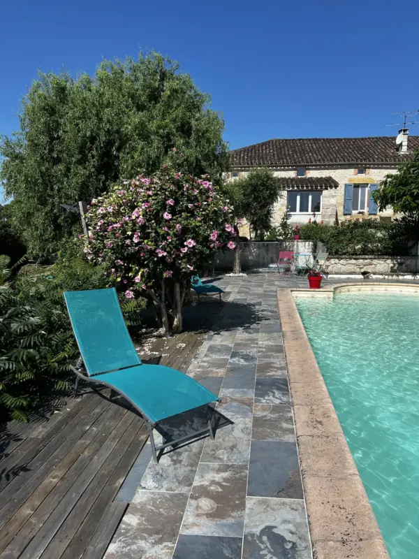 Piscine ensoleillée avec transat turquoise et maison