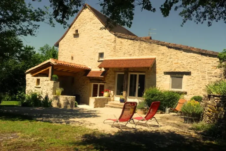 Maison en pierre avec chaises longues au jardin.