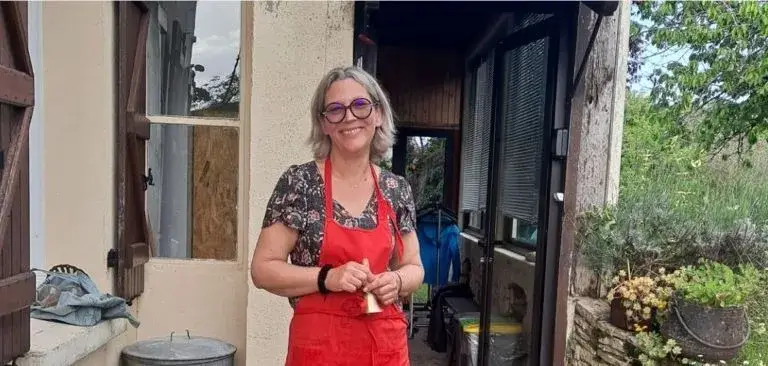 Femme souriante en tablier rouge devant maison